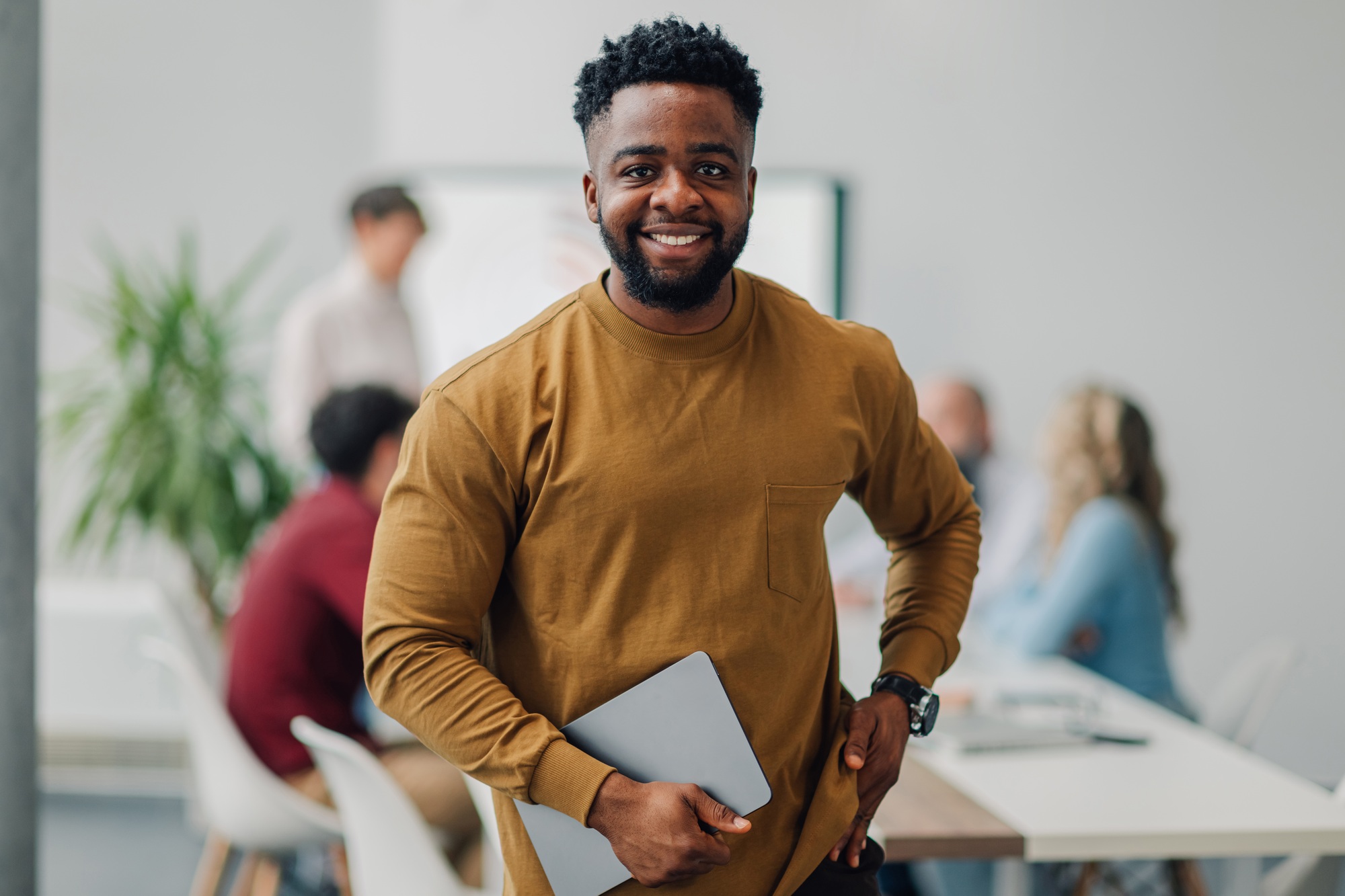 Smiling black businessman holding laptop in office meeting room